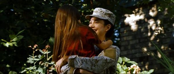 A smiling mother in Army fatigues embraces her daughter.